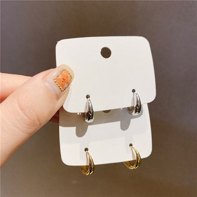 Stacked gold and silver thick teardrop hoops on display cards held in hand