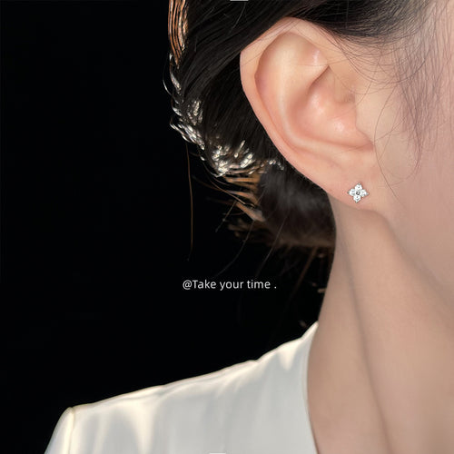 Silver-tone mini-clear-stone four-petal-flower studs shown worn on an ear.