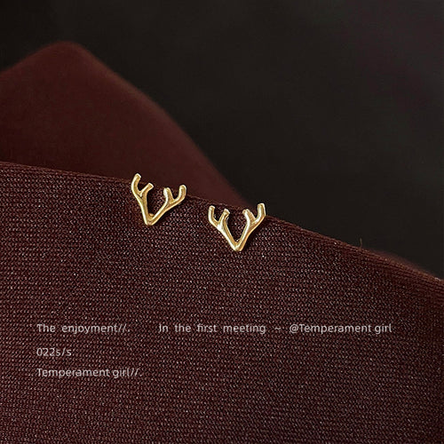 Gold antler branch studs resting on dark fabric edge