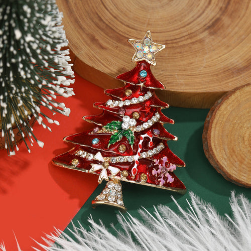 Red enamel Christmas tree brooch with star topper beside wood slices