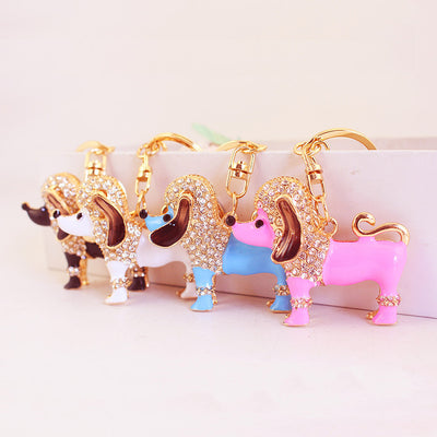 Four gold-tone poodle keychains in pink, blue, white, and black stand together.