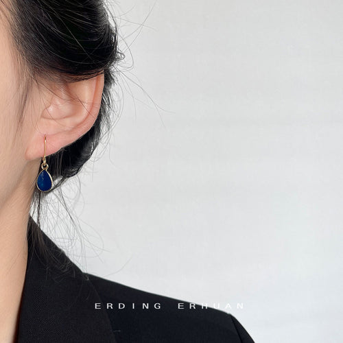Model wearing gold dark blue teardrop hook earring on left earlobe