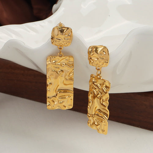 Pair of gold hammered rectangle drop earrings on white ceramic