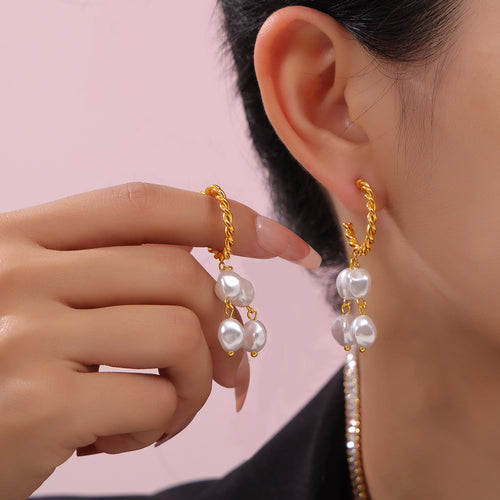 Model wearing gold twisted pearl drop stud and holding matching earring