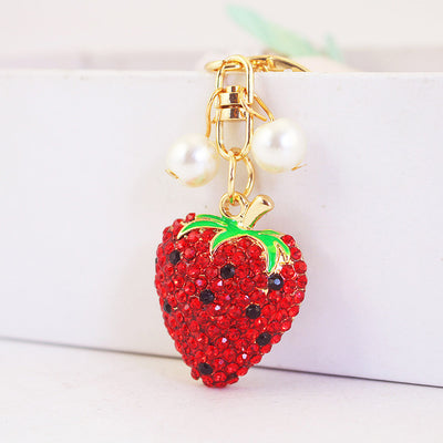 Close-up of a red rhinestone strawberry charm hanging beside two pearl-like beads.