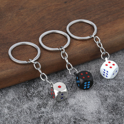Three dice keychains in black, silver, and white displayed on gray fabric.