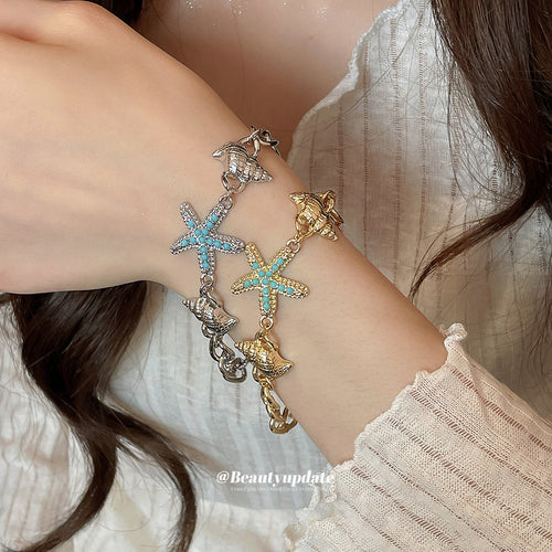 Model wearing silver and gold starfish shell charm bracelets stacked