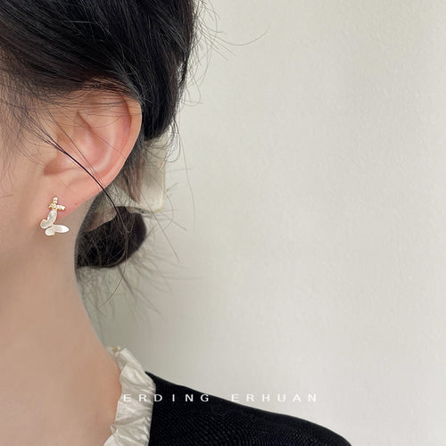 Gold-tone white-butterfly clear-stone huggie hoops shown worn on an ear.
