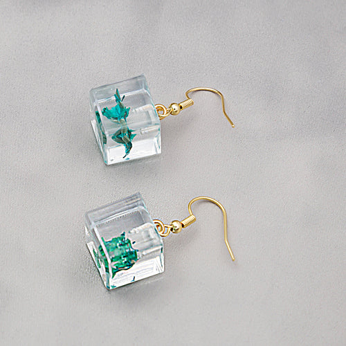 Clear resin cube green dried flower drops close-up on gray satin