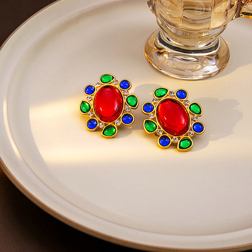 Pair of red cabochon studs with green and blue accents on cream plate