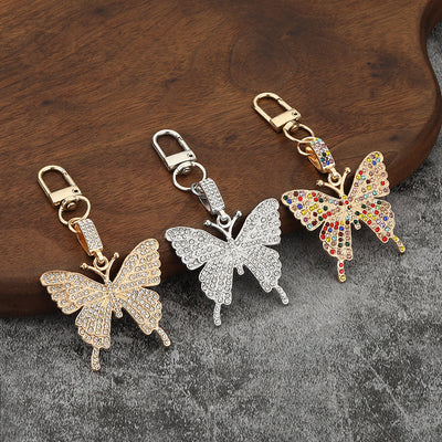Three butterfly clasp keychains in silver-tone and gold-tone finishes on a wood surface.