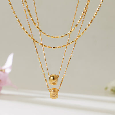Two gold double-layer rice-bead necklaces with ribbed barrel pendants hanging