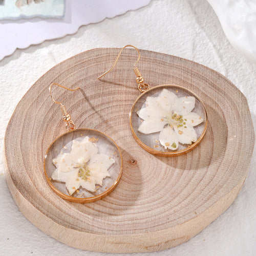 White pressed flower round gold rim earrings with gold flakes on wood
