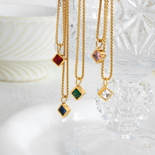 Five gold square stone pendant necklaces hanging by crystal glassware