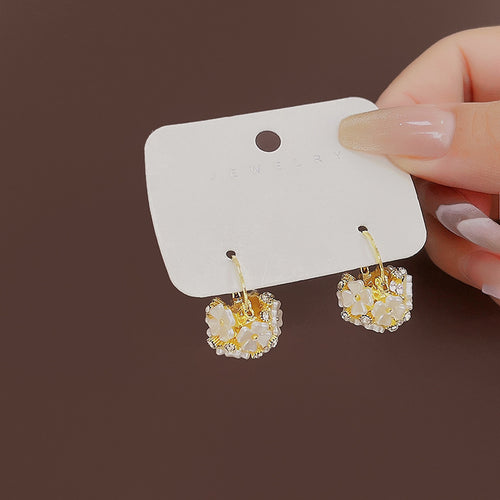 Gold flower basket hoop earrings held on white jewelry card by hand