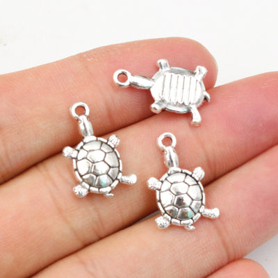 Hand held view of the detailed turtle animal charms showing the front shape and finish