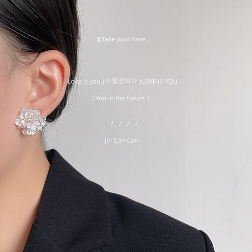 Silver-tone layered-petal sculpted flower studs shown worn on an ear.