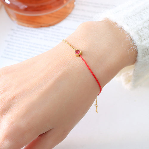 Wrist wearing red cord and gold chain bracelet with red stone