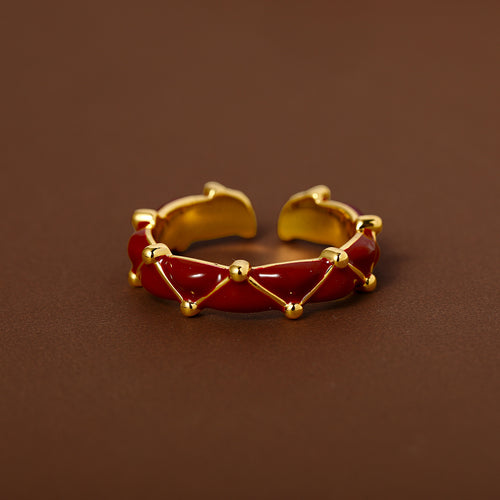Red enamel gold lattice open ring product on brown backdrop