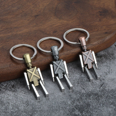 Three robot keychains in bronze-tone, silver-tone, and copper-tone finishes rest beside a wooden board.