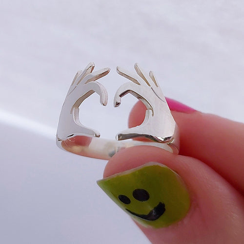 Silver tone heart hands open ring held near painted nail