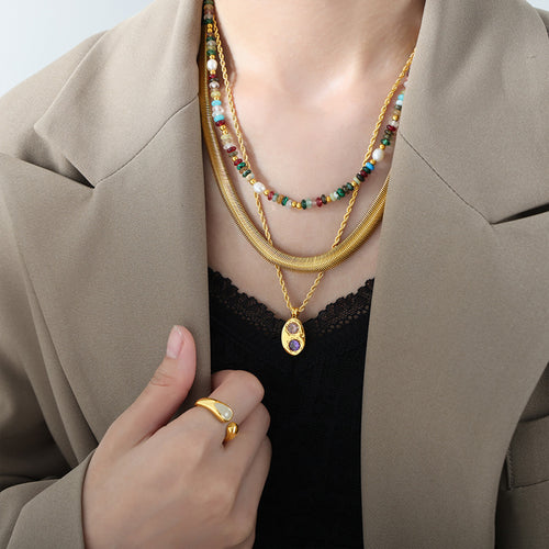 Gold flat snake chain layered with other necklaces under beige blazer