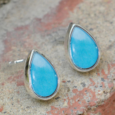 Light blue teardrop stud earrings on rough stone surface outdoor light