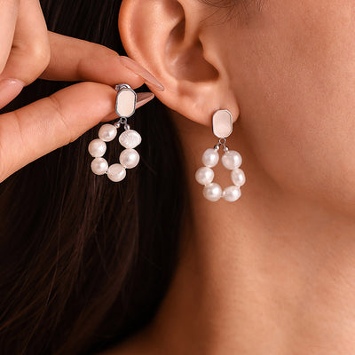 Model holding matching pearl loop shell stud earring beside ear