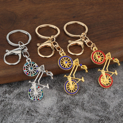 Three bicycle keychains in gold-tone and silver-tone finishes with multicolor, blue, and red stones.