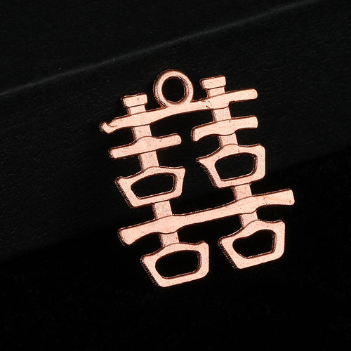 Close-up of a rose gold-tone double happiness charm on a black box edge