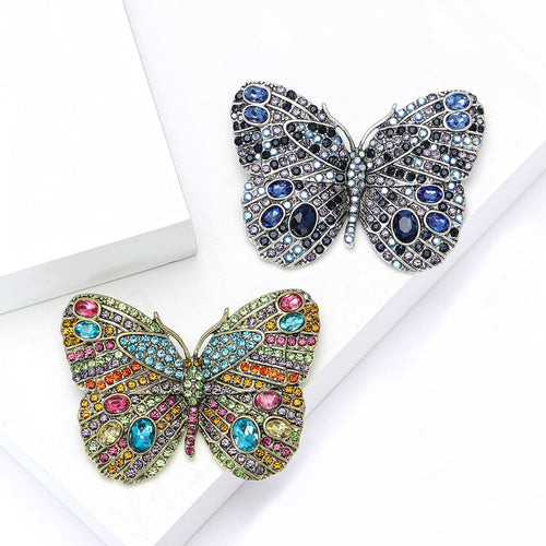 Multicolor and blue rhinestone butterfly brooches displayed on white stepped blocks