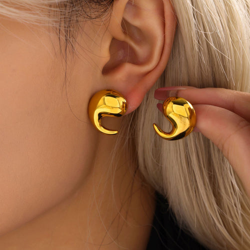 Model wearing gold swirl teardrop stud, second held beside ear