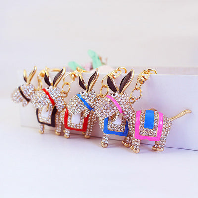 Four gold-tone donkey keychains with black, red, blue, and pink saddle accents arranged in a row.