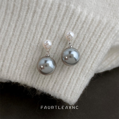 White and gray pearl drop studs resting on white knit sweater