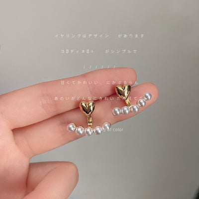 Gold-tone heart-top white-pearl row ear-jacket studs held in a hand.