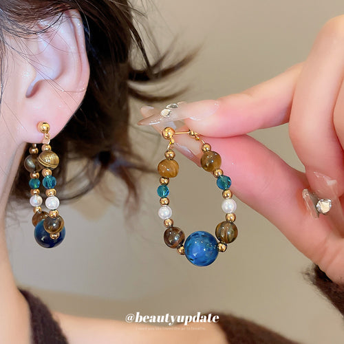 blue and brown beaded hoop drop earrings with metal tone details shown in an on-ear styling view