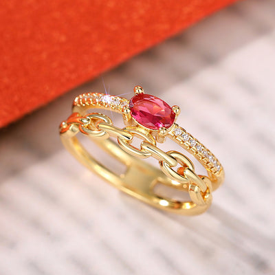 Gold dual-band ring with pink oval stone and chain links on marble