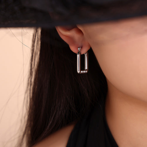 Silver rectangle hoop earring worn under black hat
