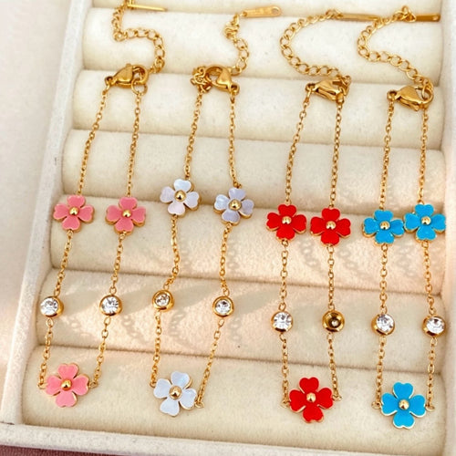 Four gold enamel flower chain bracelets hanging in cream jewelry tray