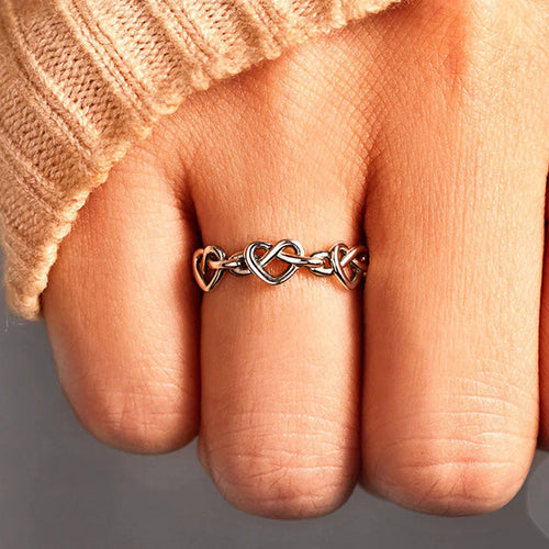 White gold heart-link ring worn on finger with beige knit cuff