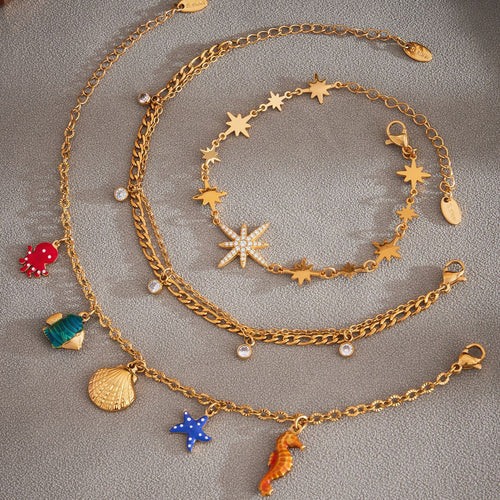 Gold ocean charms, dual figaro zircon, and star bracelets flat on gray fabric