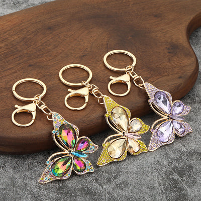 Three gold-tone butterfly keychains in multicolor, yellow, and purple finishes on a wooden surface.