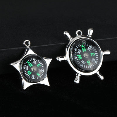 Two silver-tone compass charms, a star shape and a ship's wheel shape, on a dark background