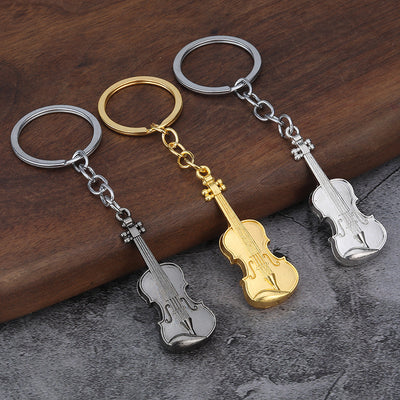 Gold, bright silver, and dark silver violin keychains arranged on wood.