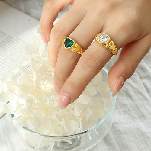 Hand wearing gold heart rings with green and clear glass stones