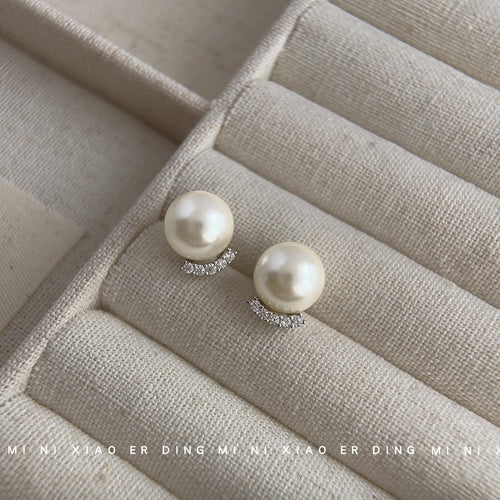 Cream pearl studs with silver crescent pavé on beige jewelry tray